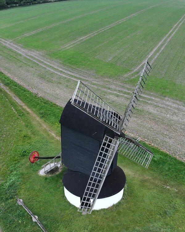 Aerial view of a traditional black weatherboarded post mill in open arable farmland — a Critical Asset heritage-asset survey