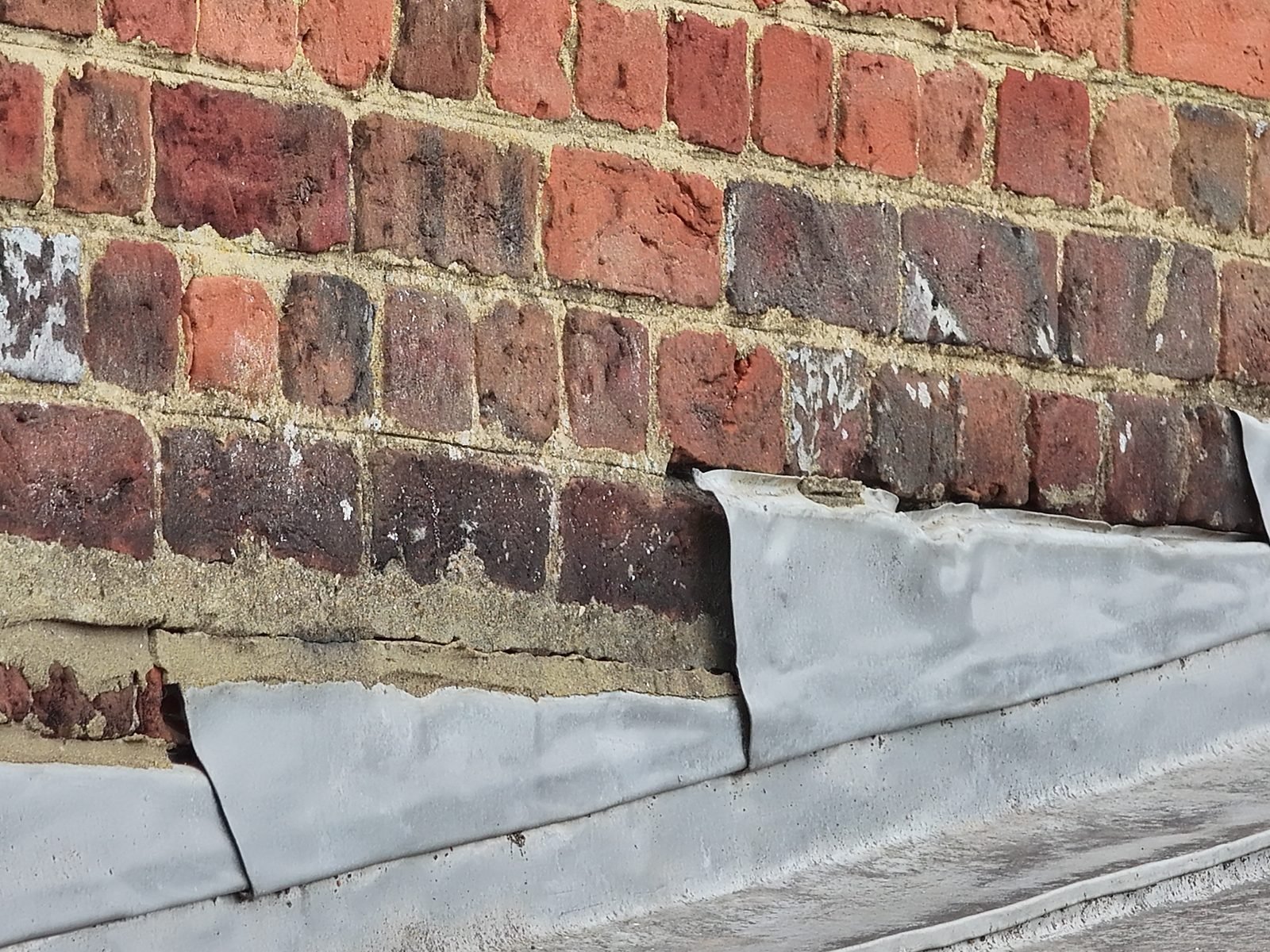 Close-range drone photograph at St Peter&rsquo;s, Chalfont St Peter, where the upper edges of stepped lead flashings stand clear of the brick face above a lead-lined gutter