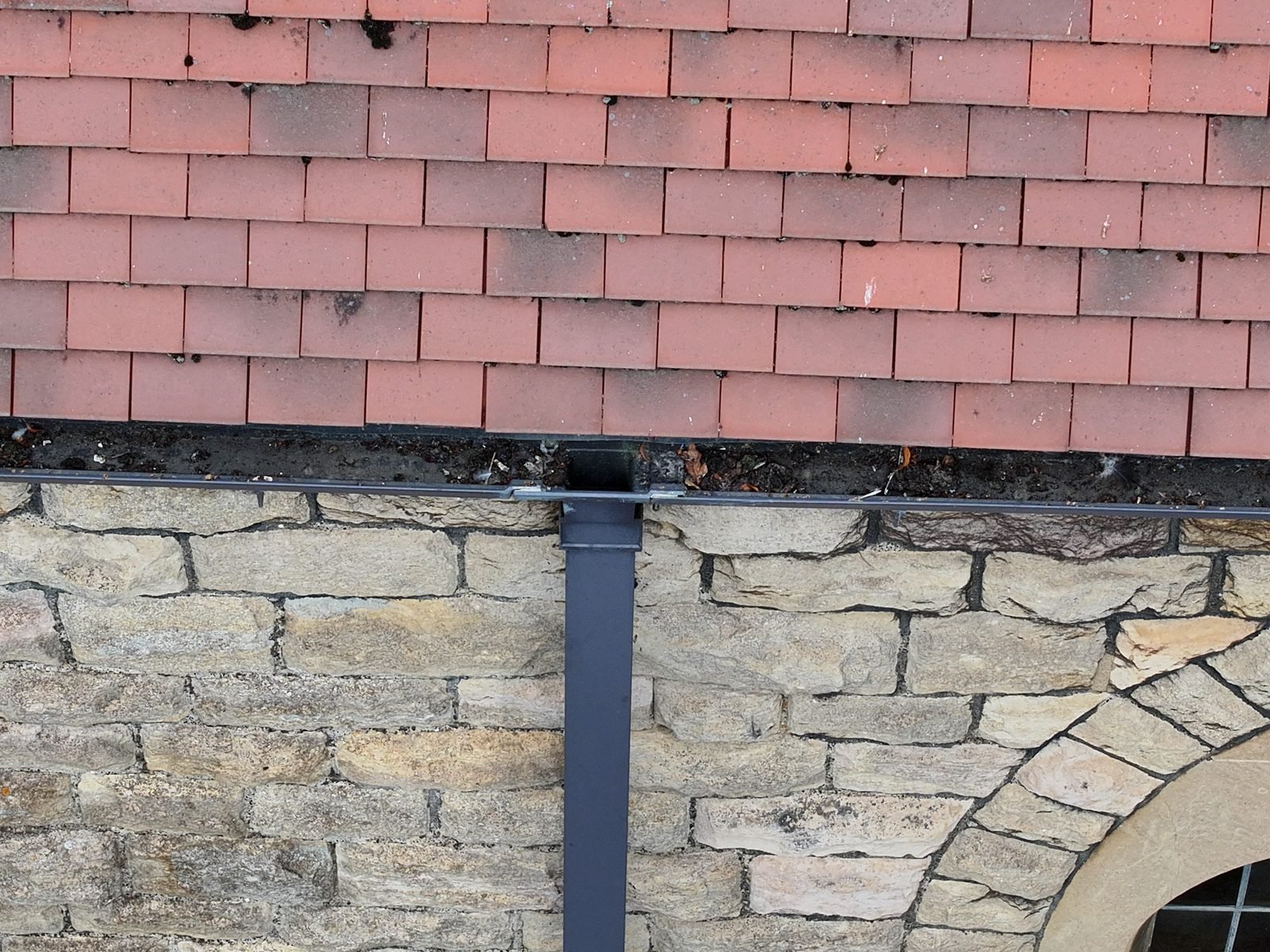 Drone photograph of an eaves gutter at St Peter&rsquo;s, March, with dark debris standing above the gutter edge beside a downpipe, over rock-faced stonework