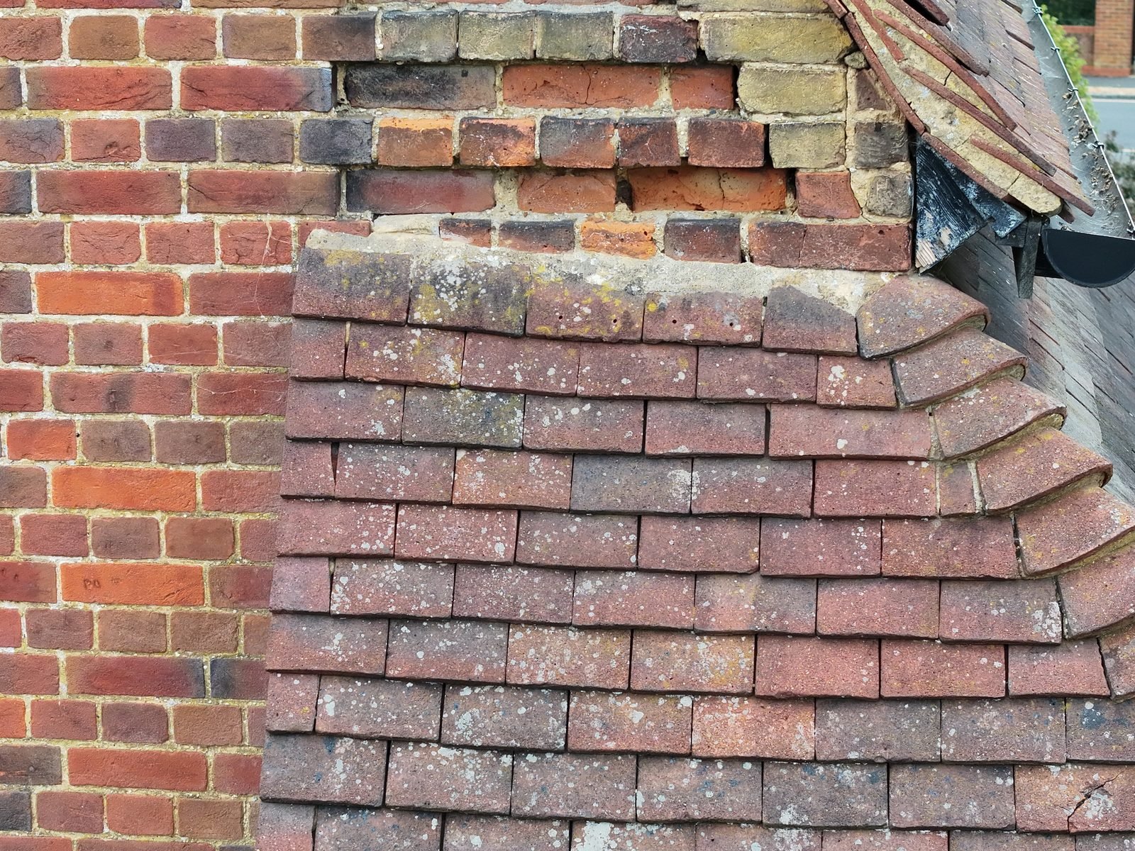 Close-range drone photograph of plain-tiled courses meeting brickwork at All Saints, Chalfont St Peter, with open joints visible in the brick above