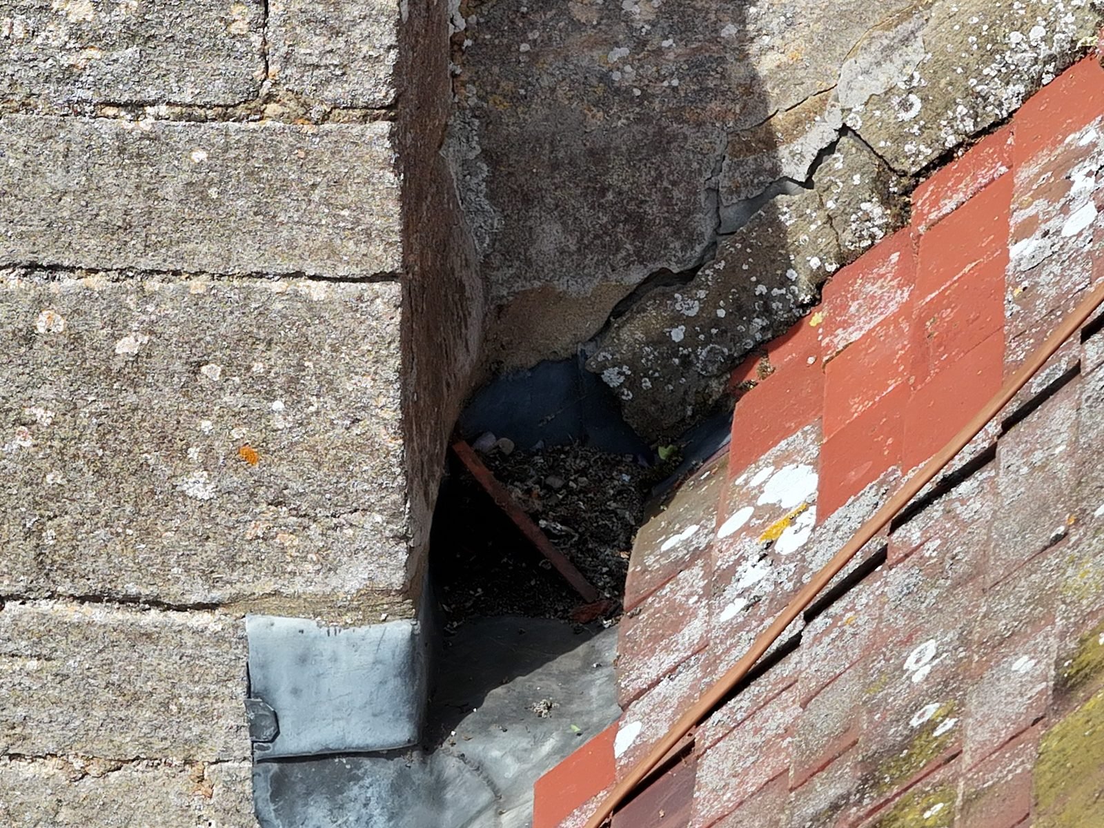 Close-range drone photograph of the junction between the tiled roof slope and the tower at St Thomas à Becket church, Ramsey, showing the mortar fillet, debris and lead soakers