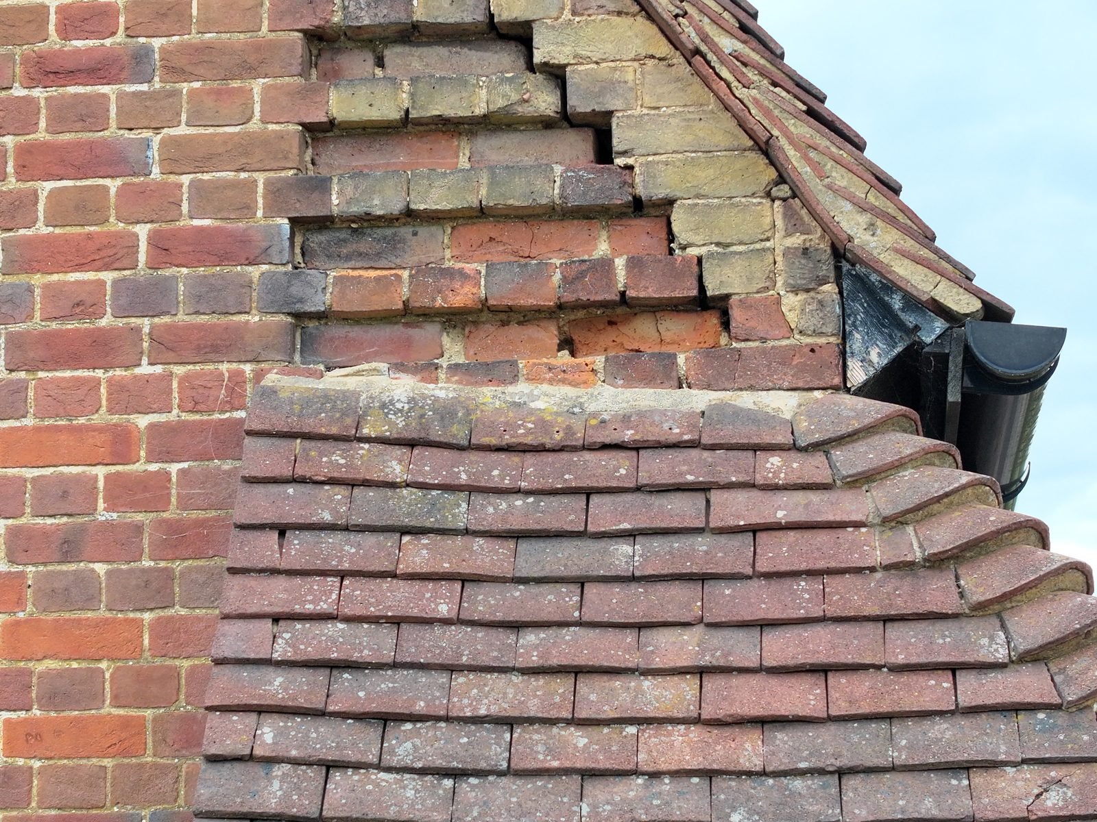 Close-range drone photograph of a church gable where the tiled roof abuts brickwork, showing open mortar joints and displaced bricks above the abutment
